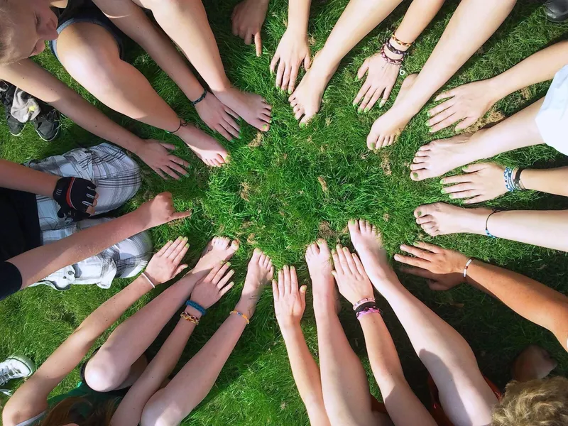 A circle of hands and bare feet on grass, seen from directly above