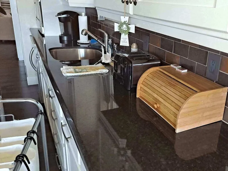A kitchen counter with a coffee maker, toaster, sink and bamboo bread box