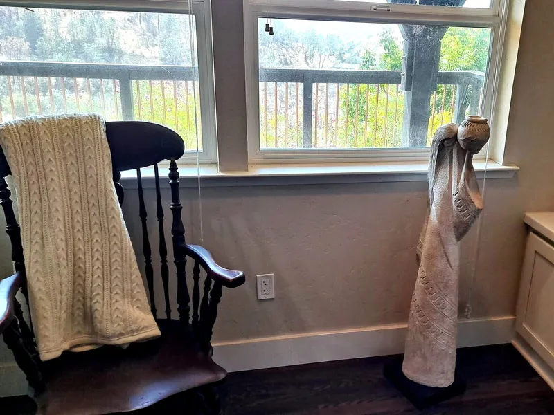 A rocking chair with a knitted throw beside a window at the residence