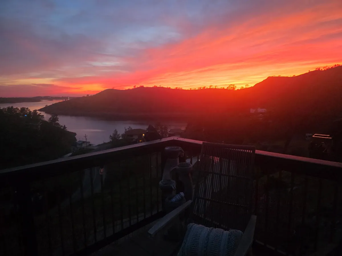 A red sunset over Millerton Lake, seen past the chair on the deck