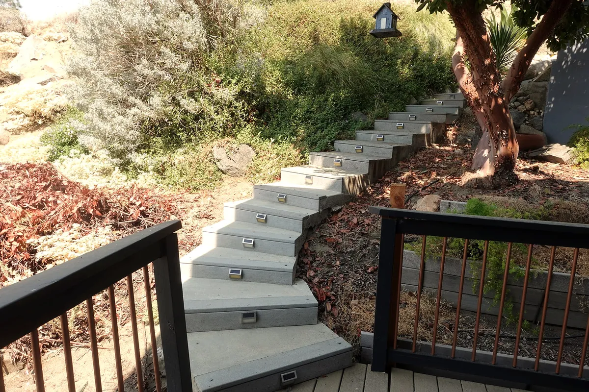 Concrete garden steps with path lights climbing the hillside at the residence